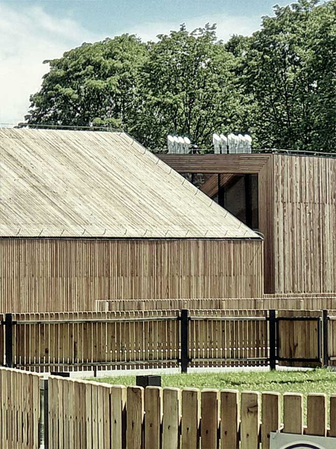 Zdjęcie przedstawia fragment architektury Służewskiego Domu Kultury. Drewniane budynki oraz płot i fragment amfiteatru.