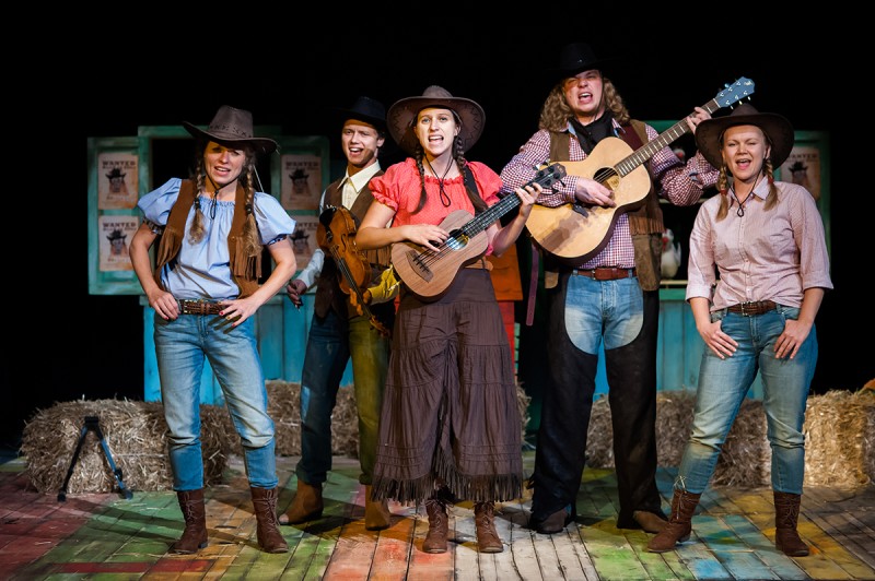 Zdjęcie przedstawia stojąca grupę aktorów i aktorek stylizowanych na cowboy'ów, niektórzy z nich trzymają gitary, inni mają otwarte usta.