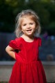 Na zdjęciu widać małą uśmiechniętą dziewczynkę w czerwonej sukience. W tle widać amfiteatr SDK. 