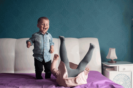  Na zdjęciu widać 2-letniego śmiejącego się chłopca po lewej, po prawej widać 4-letnią dziewczynkę robiącą fikołka na łóżku. fot. Zuzanna Jach
