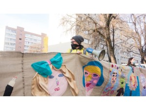 Portrety mokotowskich wolontariuszy podczas przemarszu przez Służew. W tle bloki z wielkiej płyty