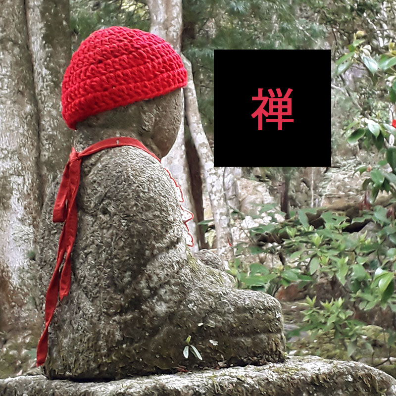 Na zdjęciu kamienny posąg Buddy w robionrj na szydełku czerwonej czapce. Na zdjęciu czarny kwadrat z napisem japońskim Zen. Fot. Agnieszka Kmieciak