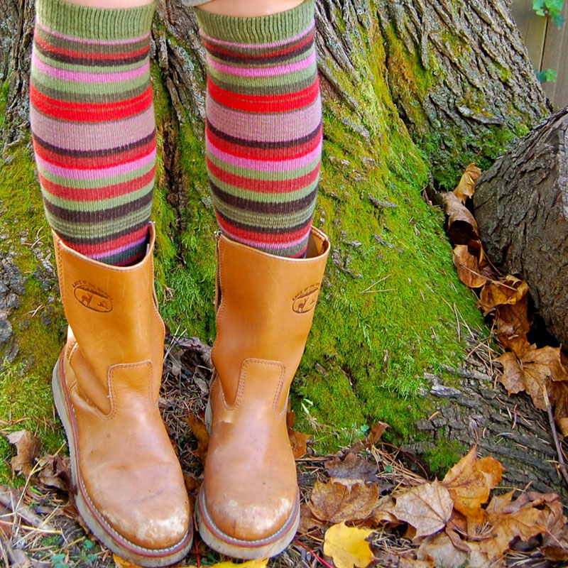 Kwadratowe zdjęcie: Na tle omszałego drzewa dziecięce nogi w kolorowych podkolanówkach.